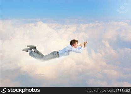 Business break. Young businessman flying in sky and playing fife