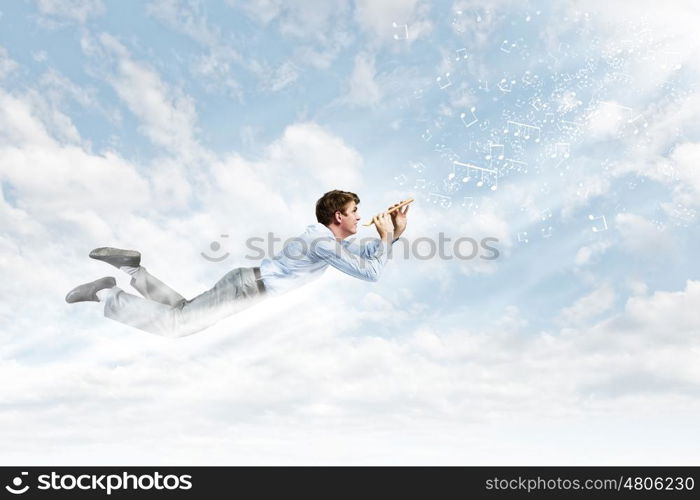 Business break. Young businessman flying in sky and playing fife