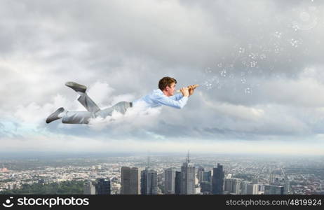 Business break. Young businessman flying in sky and playing fife