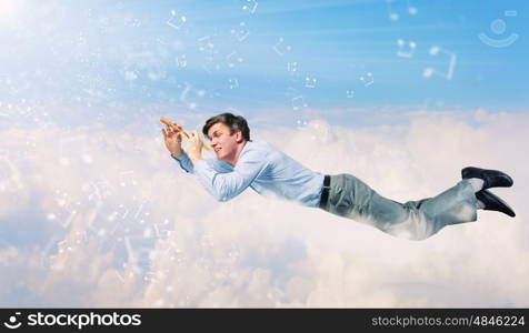 Business break. Young businessman flying in sky and playing fife