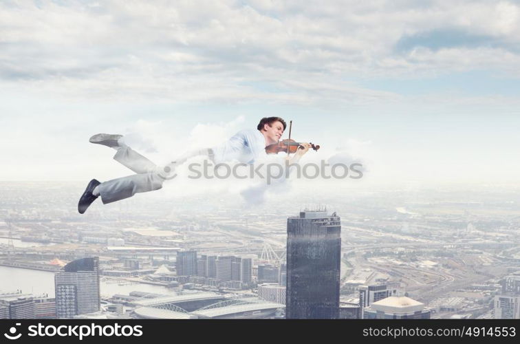 Business break. Young businessman flying in sky and playing violin