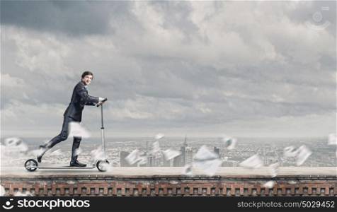 Business break. Young businessman riding scooter on roof of building