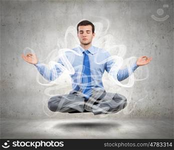 Business break. Young businessman sitting in lotus pose and meditating