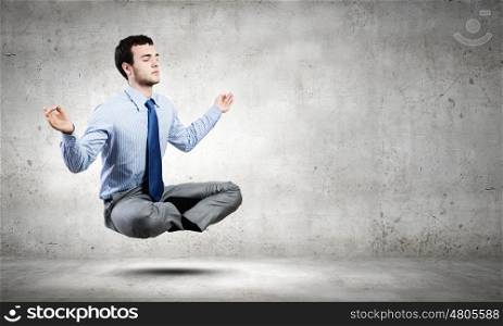 Business break. Young businessman sitting in lotus pose and meditating