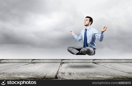 Business break. Young businessman sitting in lotus pose and meditating