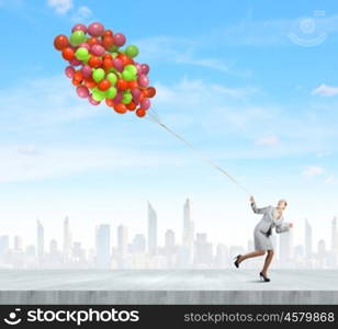 Business break. Young businesswoman running with bunch of colorful balloons