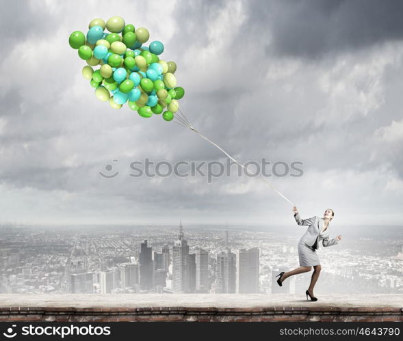 Business break. Young businesswoman running with bunch of colorful balloons