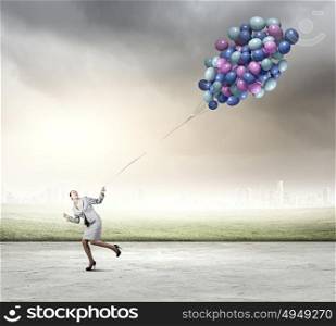 Business break. Young businesswoman running with bunch of colorful balloons