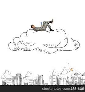 Business break. Young relaxed businessman lying on cloud and reading book