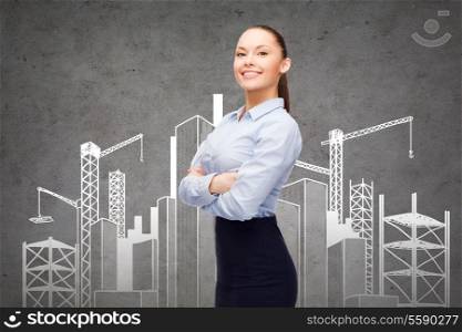 business, building and education concept - friendly young smiling businesswoman with crossed arms and construction site on the back