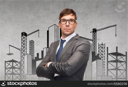 business, building and office concept - attractive businessman or teacher in glasses with construction site on the back