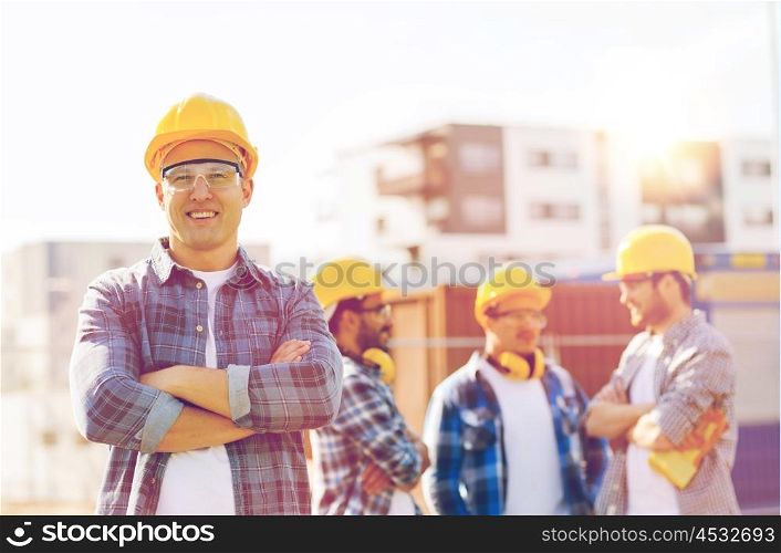 business, building, construction and people concept - group of smiling builders in hardhats outdoors