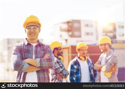 business, building, construction and people concept - group of smiling builders in hardhats outdoors