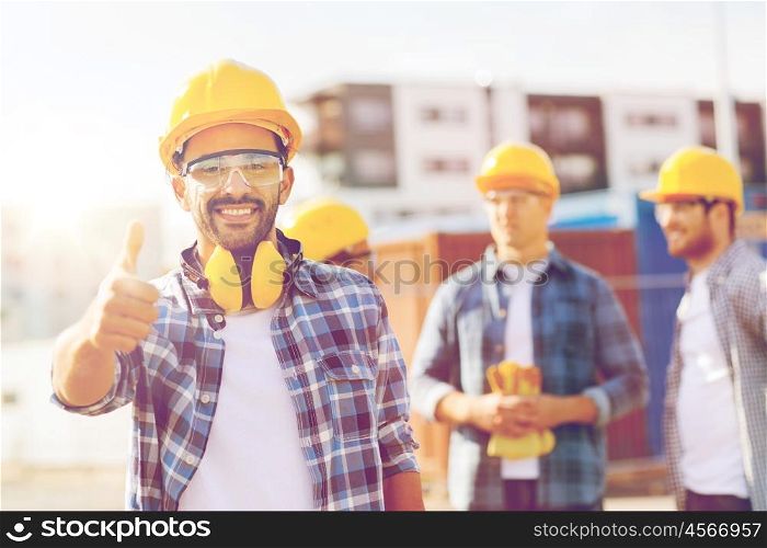 business, building, construction, gesture and people concept - group of smiling builders in hardhats showing thumbs up outdoors