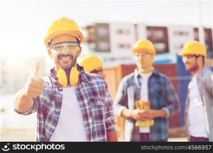 business, building, construction, gesture and people concept - group of smiling builders in hardhats showing thumbs up outdoors