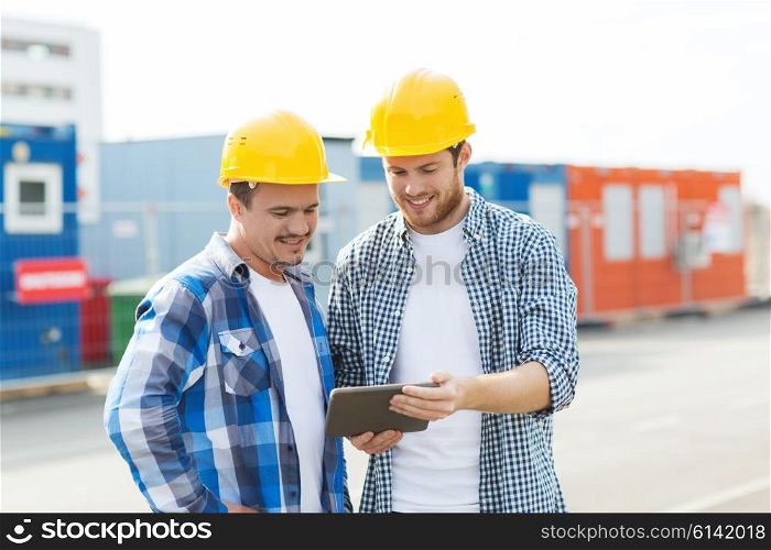 business, building, construction, technology and people concept - two smiling builders in hardhats looking at tablet pc computer outdoors