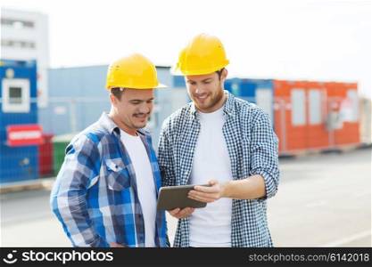 business, building, construction, technology and people concept - two smiling builders in hardhats looking at tablet pc computer outdoors