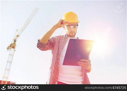 business, building, paperwork and people concept - builder in hardhat with clipboard outdoors