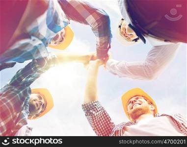 business, building, partnership, gesture and people concept - close up of smiling builders in hardhats making high five outdoors