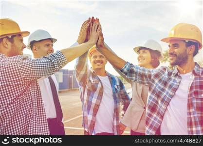 business, building, partnership, gesture and people concept - close up of smiling builders and architects in hardhats making high five outdoors