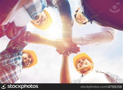 business, building, partnership, gesture and people concept - close up of smiling builders in hardhats with hands on top outdoors