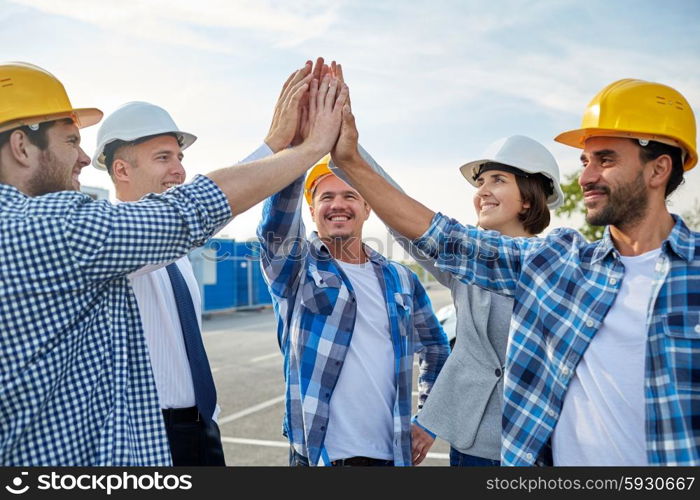 business, building, partnership, gesture and people concept - close up of smiling builders and architects in hardhats making high five outdoors