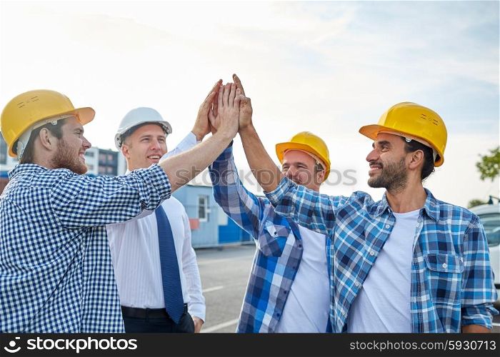 business, building, partnership, gesture and people concept - close up of smiling builders and architect in hardhats making high five outdoors