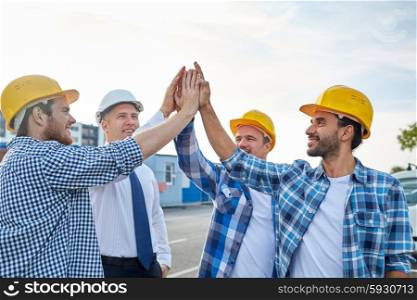 business, building, partnership, gesture and people concept - close up of smiling builders and architect in hardhats making high five outdoors