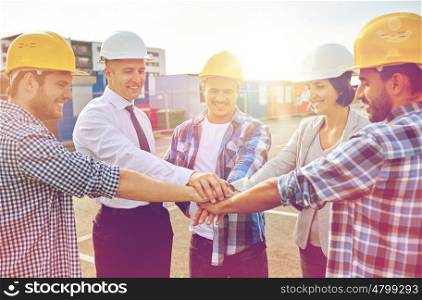 business, building, partnership, gesture and people concept - smiling builders and architects in hardhats with hands on top outdoors