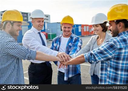 business, building, partnership, gesture and people concept - smiling builders and architects in hardhats with hands on top outdoors