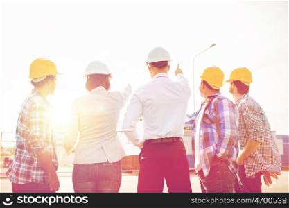 business, building, teamwork and people concept - group of builders and architects in hardhats with blueprint on construction site