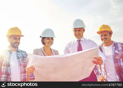 business, building, teamwork and people concept - group of builders and architects in hardhats with blueprint on construction site