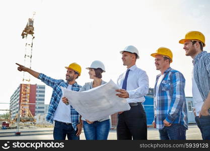 business, building, teamwork and people concept - group of builders and architects in hardhats with blueprint on construction site