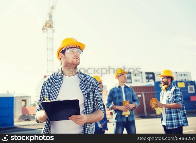 business, building, teamwork and people concept - group of builders in hardhats with clipboard outdoors