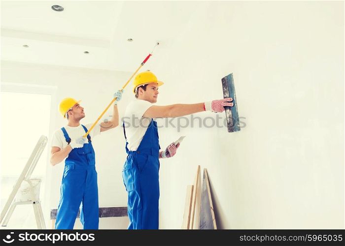 business, building, teamwork and people concept - group of builders in hardhats with plastering tools indoors