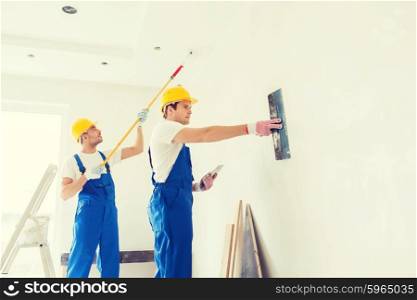 business, building, teamwork and people concept - group of builders in hardhats with plastering tools indoors