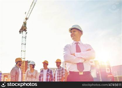 business, building, teamwork and people concept - group of smiling builders and architect in hardhats at construction site