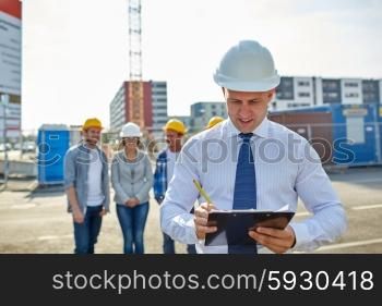 business, building, teamwork and people concept - group of smiling builders and architect with clipboard in hardhats at construction site