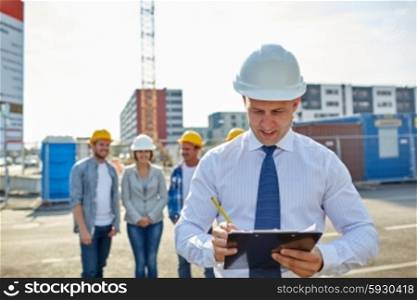 business, building, teamwork and people concept - group of smiling builders and architect with clipboard in hardhats at construction site