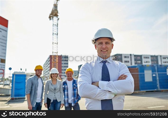business, building, teamwork and people concept - group of smiling builders and architect in hardhats at construction site