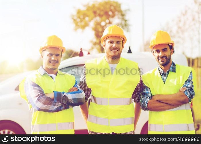 business, building, teamwork and people concept - group of smiling builders in hardhats on car background outdoors