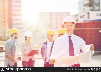business, building, teamwork and people concept - group of smiling builders in hardhats with clipboard and blueprint outdoors. group of builders with tablet pc and blueprint