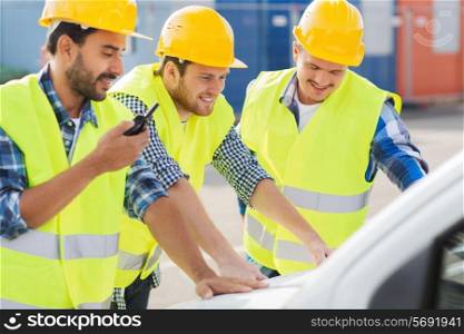 business, building, teamwork and people concept - group of smiling builders in hardhats with radio and car outdoors