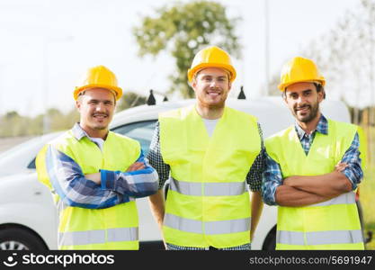 business, building, teamwork and people concept - group of smiling builders in hardhats on car background outdoors