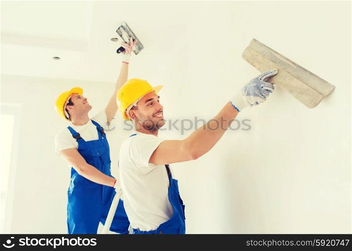 business, building, teamwork and people concept - group of smiling builders in hardhats with plastering tools indoors