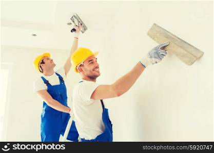business, building, teamwork and people concept - group of smiling builders in hardhats with plastering tools indoors