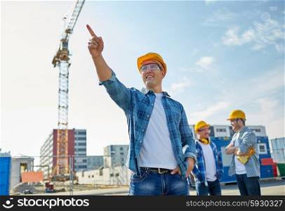 business, building, teamwork and people concept - group of smiling builders in hardhats pointing finger aside on construction site