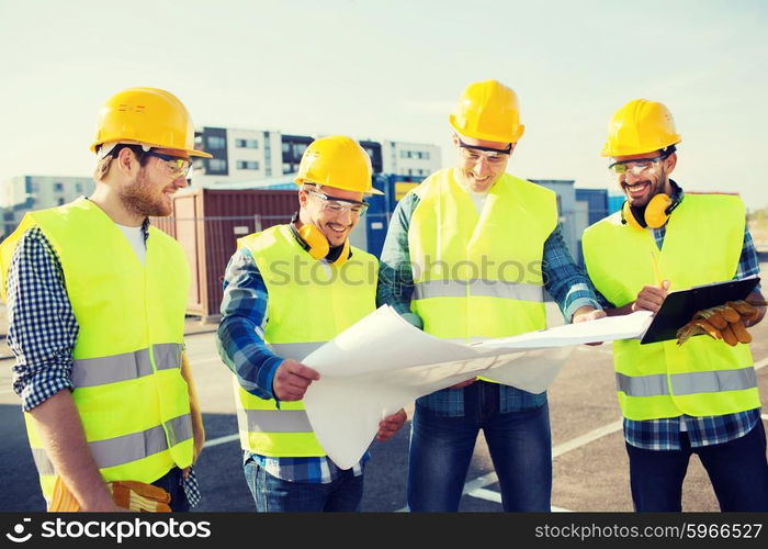 business, building, teamwork and people concept - group of smiling builders in hardhats with clipboard and blueprint outdoors