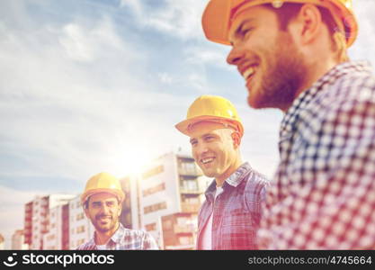 business, building, teamwork and people concept - group of smiling builders in hardhats at construction site