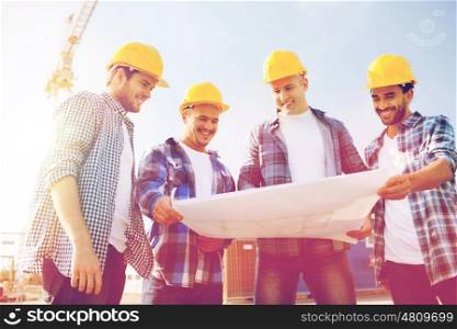 business, building, teamwork and people concept - group of smiling builders in hardhats with blueprint outdoors